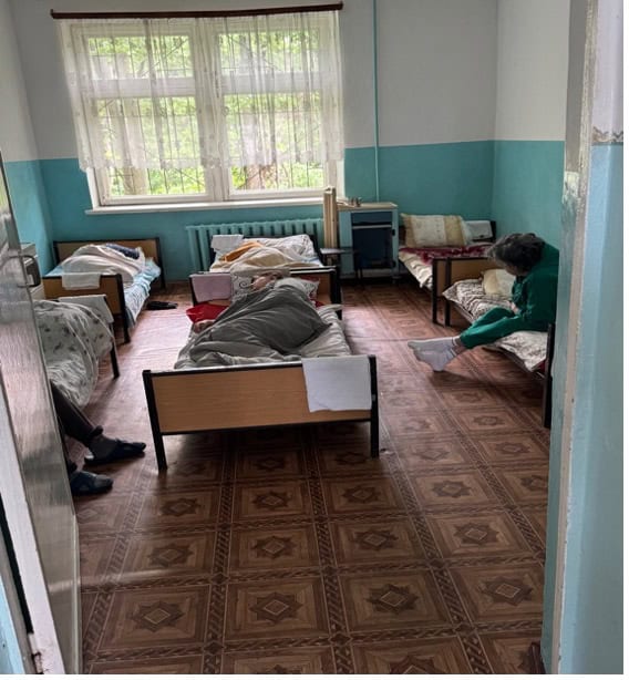 Kamer in de psychiatrische kliniek van Orhei met eenvoudige bedden en patiënten, waar opvang wordt geboden aan mensen met verslavingen en psychiatrische problemen.