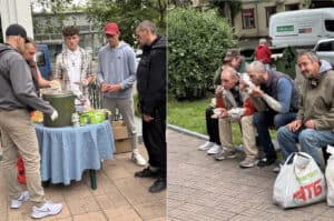 Vrijwilligers delen eten uit aan dak- en thuislozen in Odessa; enkele mannen zitten op een bankje en eten hun maaltijd, een initiatief om hulp te bieden aan mensen met verslavings- en verwaarlozingsproblematiek