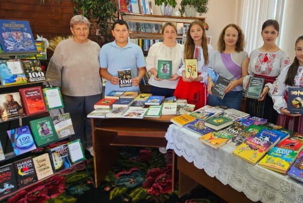 Groep vrijwilligers en lokale bewoners in Moldavische bibliotheek tijdens SMHO-hulpactie, omringd door gedoneerde boeken en educatief materiaal ter bevordering van leesvaardigheid en onderwijs in Oost-Europa.