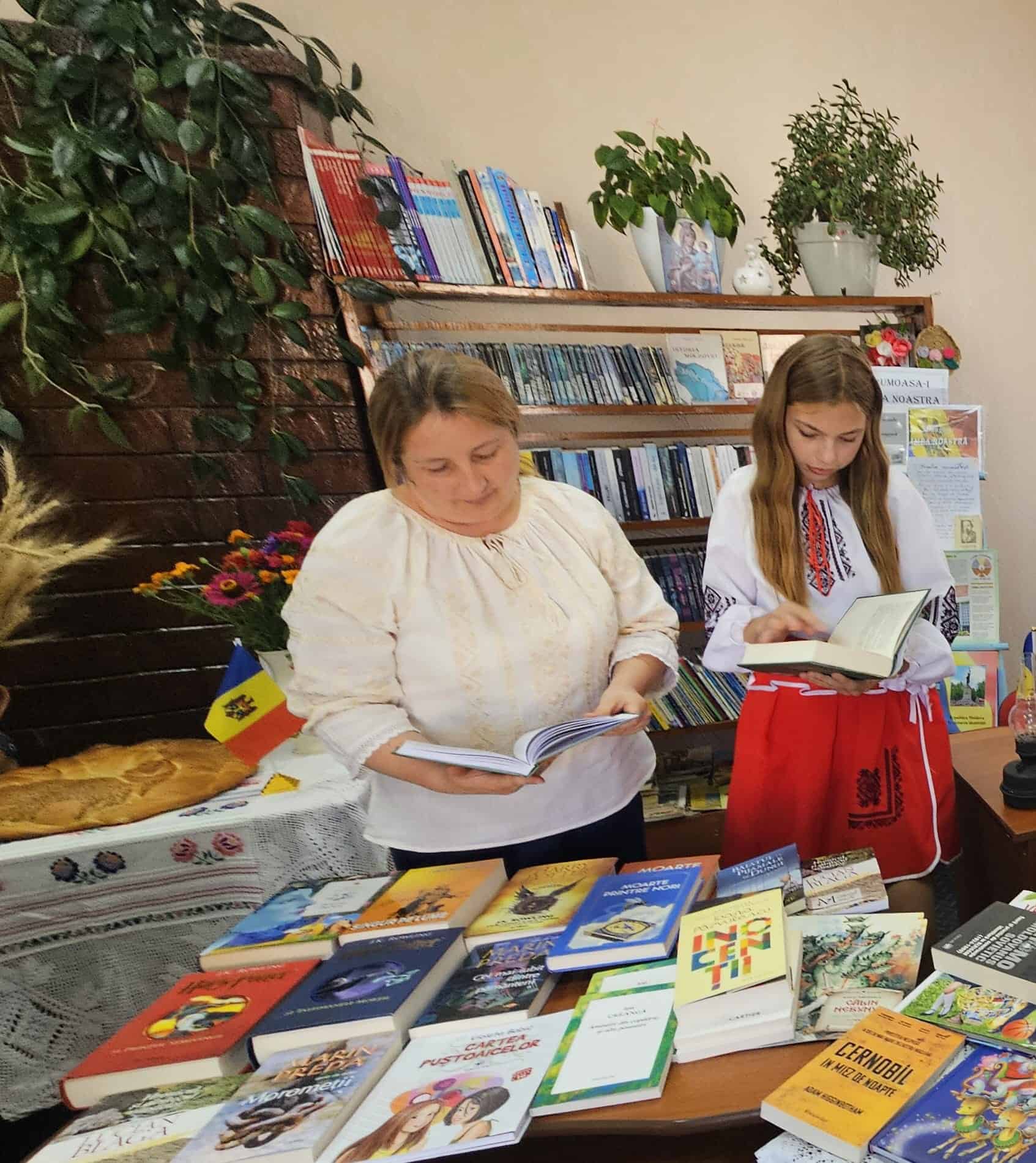 Volwassene en jong meisje in traditionele Moldavische kleding lezen boeken tijdens SMHO-hulpactie in schoolbibliotheek, met gedoneerde titels zoals Harry Potter en De Kleine Prins ter bevordering van educatie en cultuur in Oost-Europa.